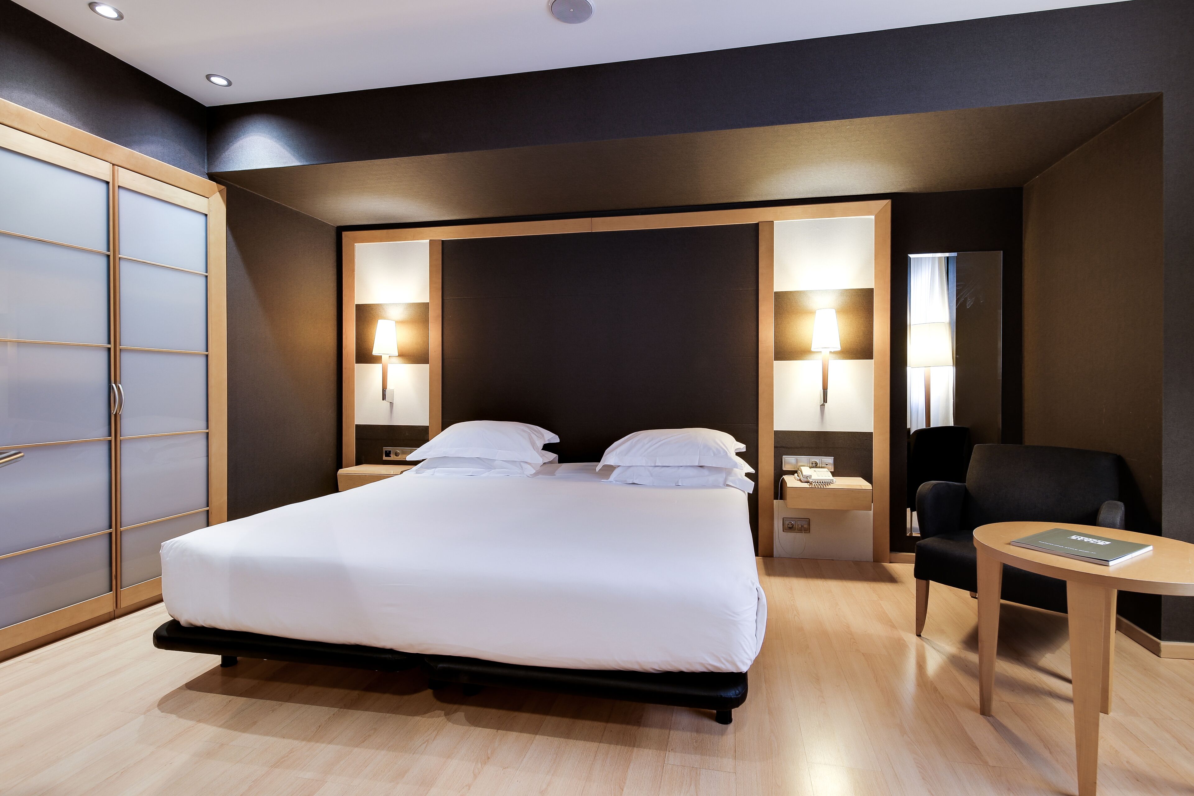 Una habitación de hotel moderna con una cama grande, lámparas de noche, un escritorio y una silla.