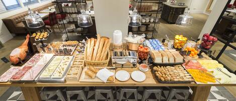 A buffet with various food items and a seating area with tables and chairs.