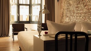 A hotel room with a bed, a desk, a chair, a lamp, and a brick wall. - 9Hotel Central (Brussels)