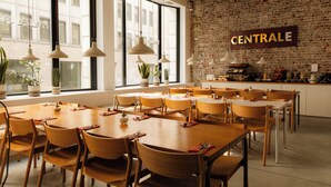 A spacious dining area with multiple tables and chairs, large windows, and a brick wall with a sign. - 9Hotel Central (Brussels)
