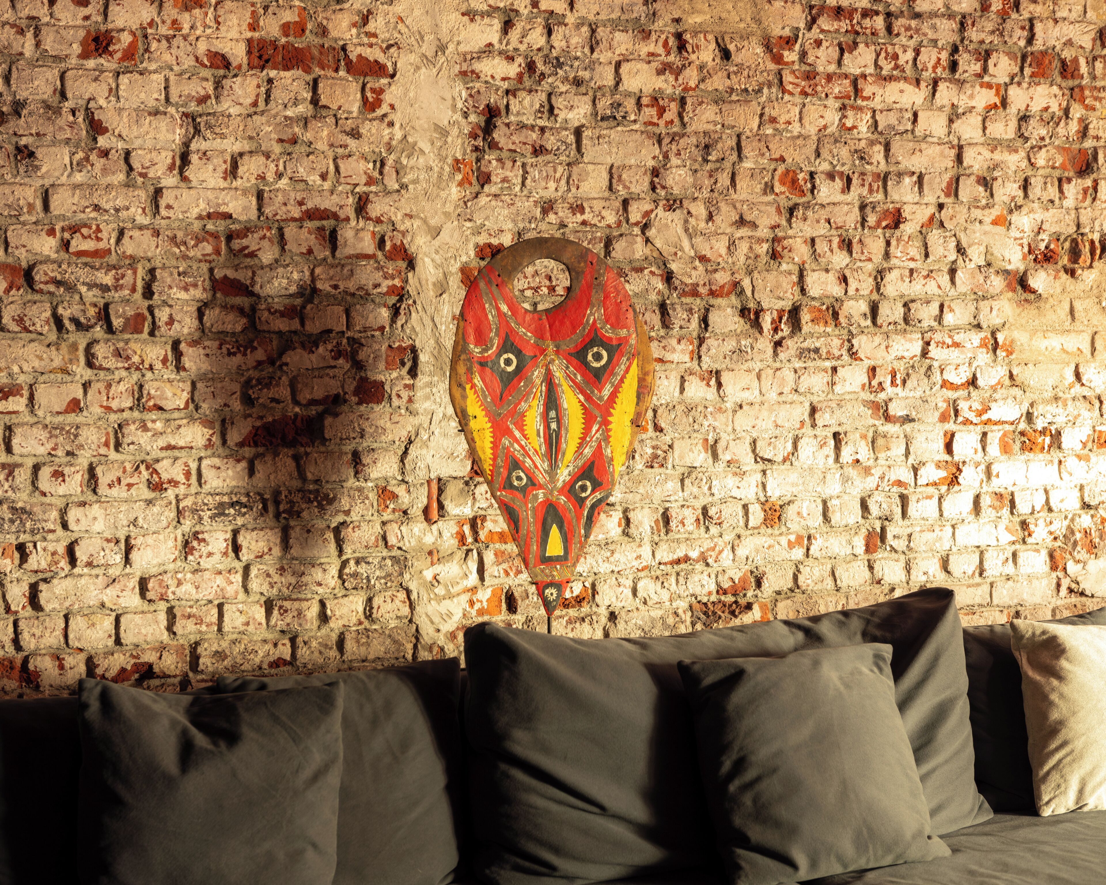 A room with a brick wall, a decorative mask, and a sofa with cushions.