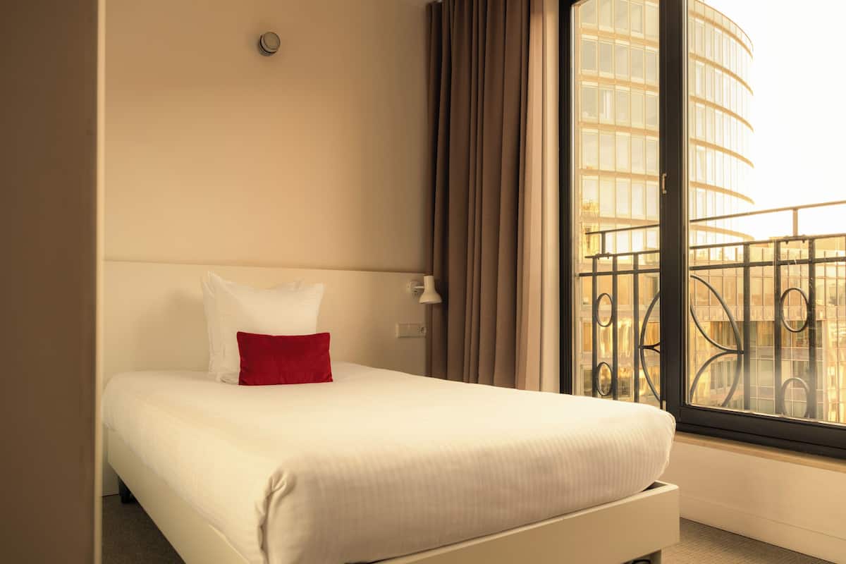 A hotel room with a bed, a window with a view of a building, and a curtain.