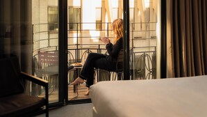 A hotel room with a bed, a sitting area with a chair and a table, and a view through a glass door to the outside. - 9Hotel Central (Brussels)