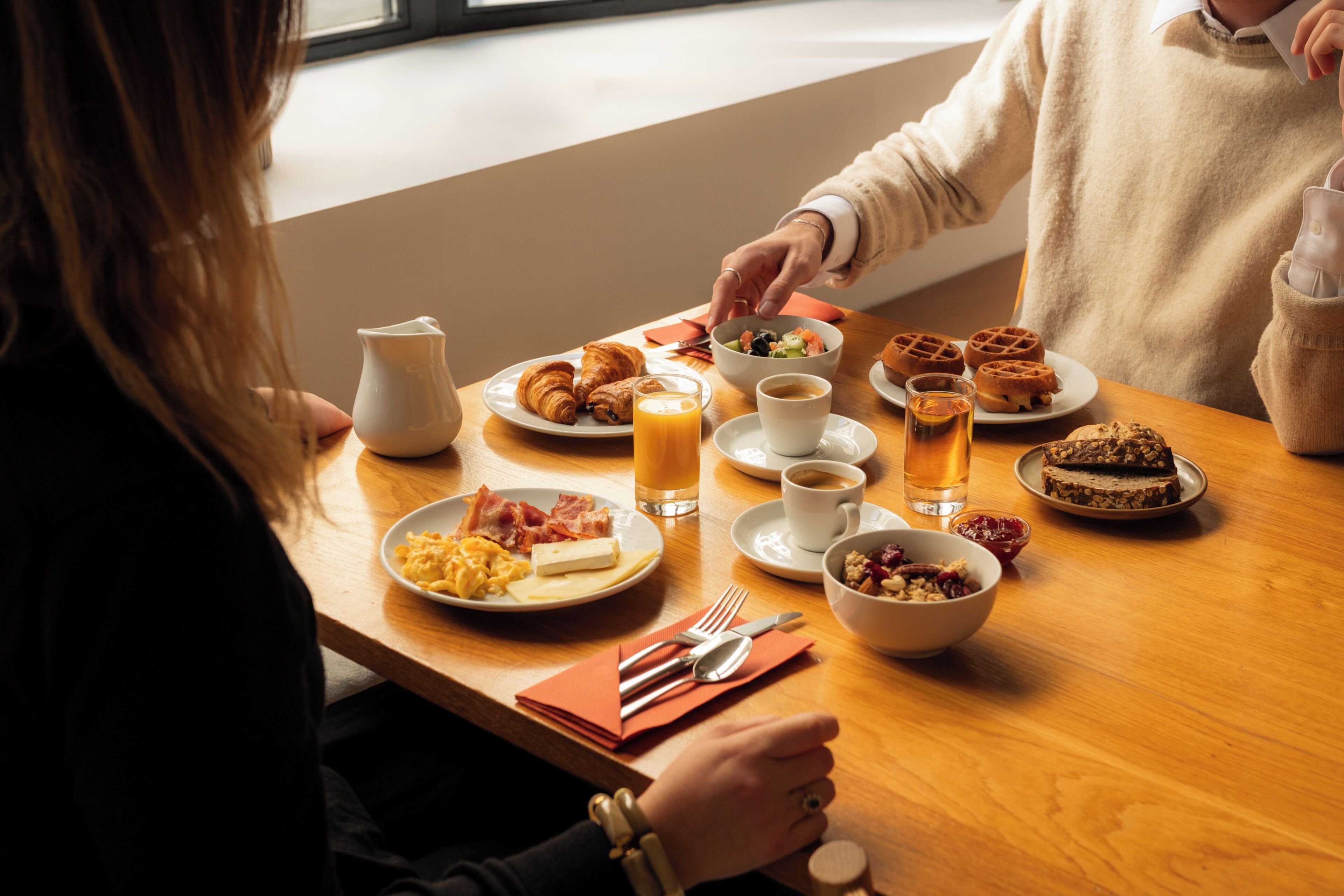 A breakfast table with plates of food, cups, and a pitcher.