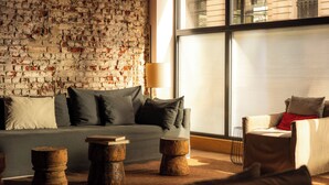 A modern living room with a brick wall, a sofa with cushions, a wooden coffee table, and a chair with a red cushion. - 9Hotel Central (Brussels)