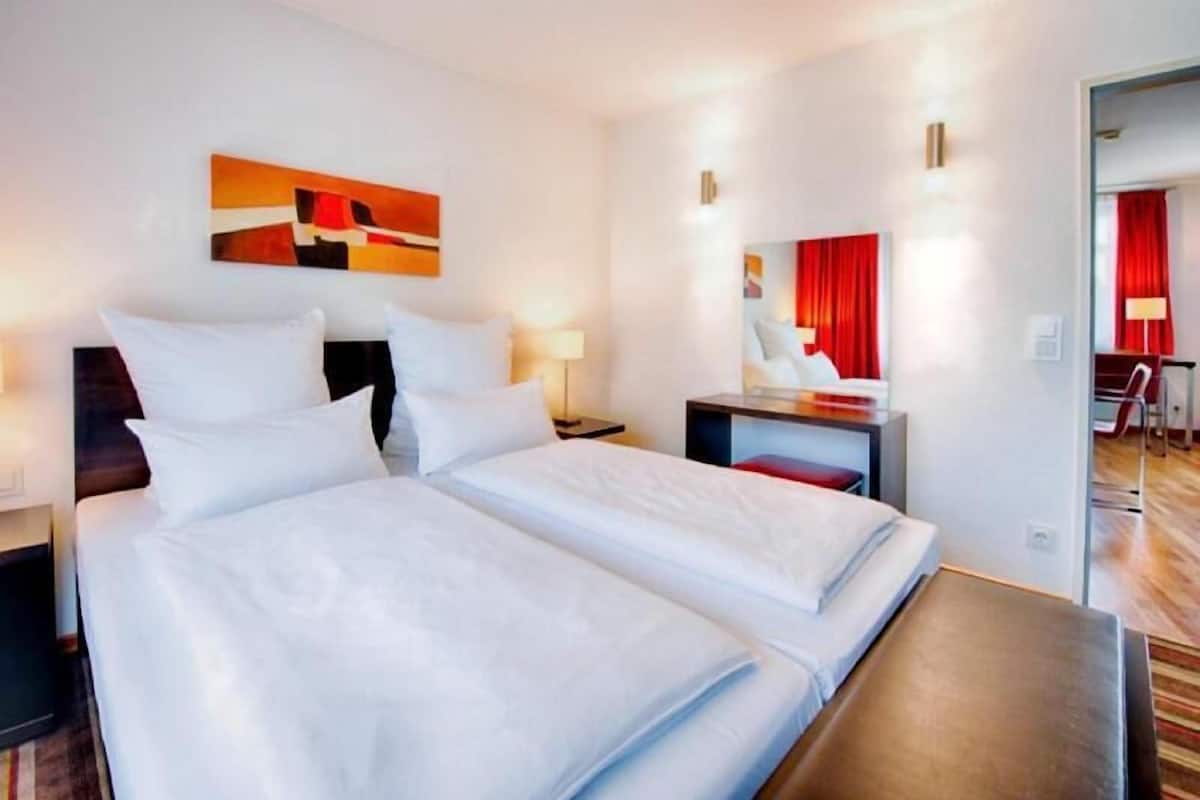 Een hotelkamer met twee bedden, een bureau, een stoel, een spiegel en een rood gordijn.
