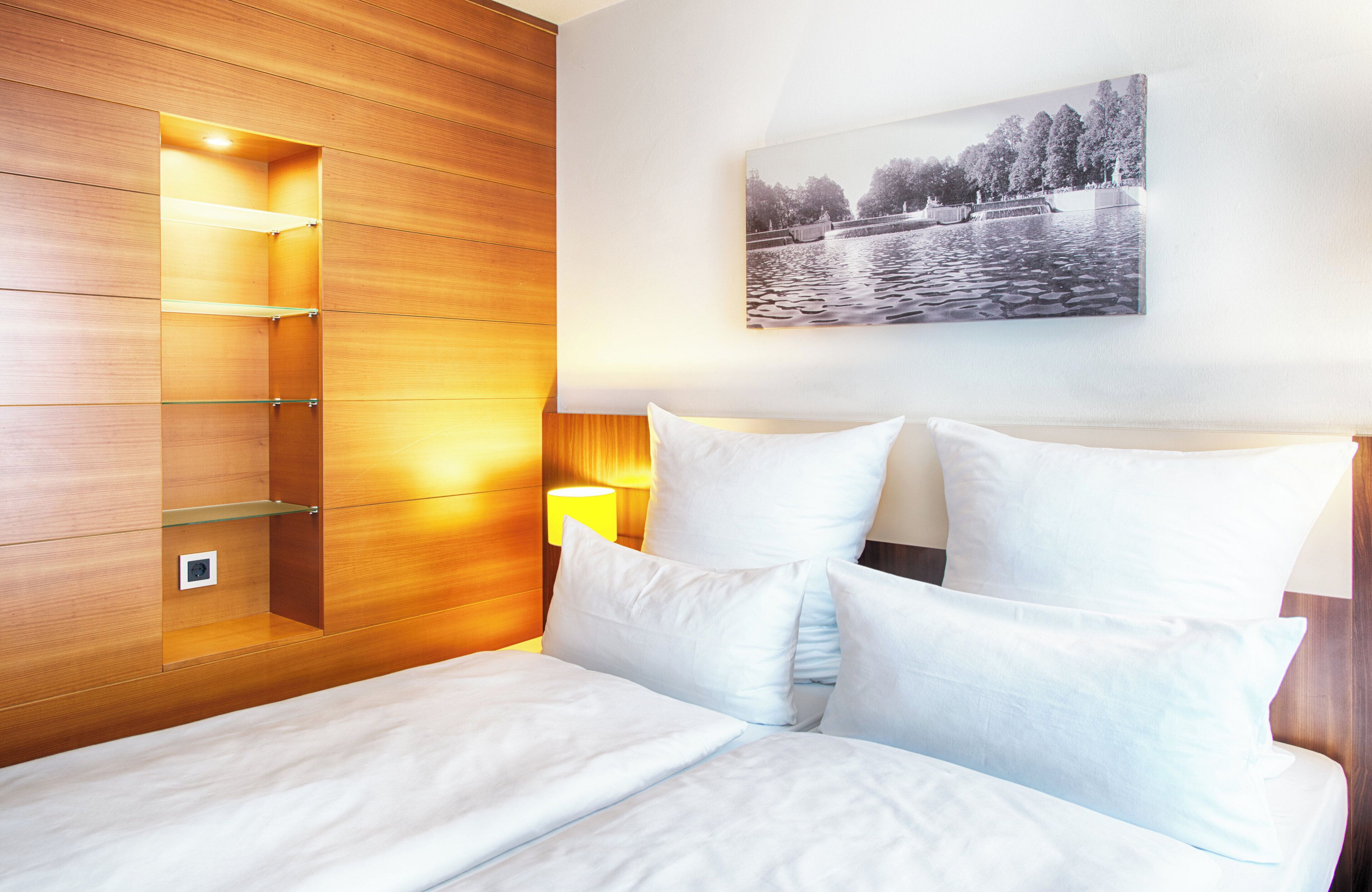 Habitación de hotel con armario de madera, cama con ropa blanca y un cuadro de un paisaje lacustre en la pared.