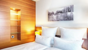 Habitación de hotel con un armario de madera, una cama con ropa de cama blanca, una mesita de noche con lámpara y una fotografía blanco y negro en la pared.