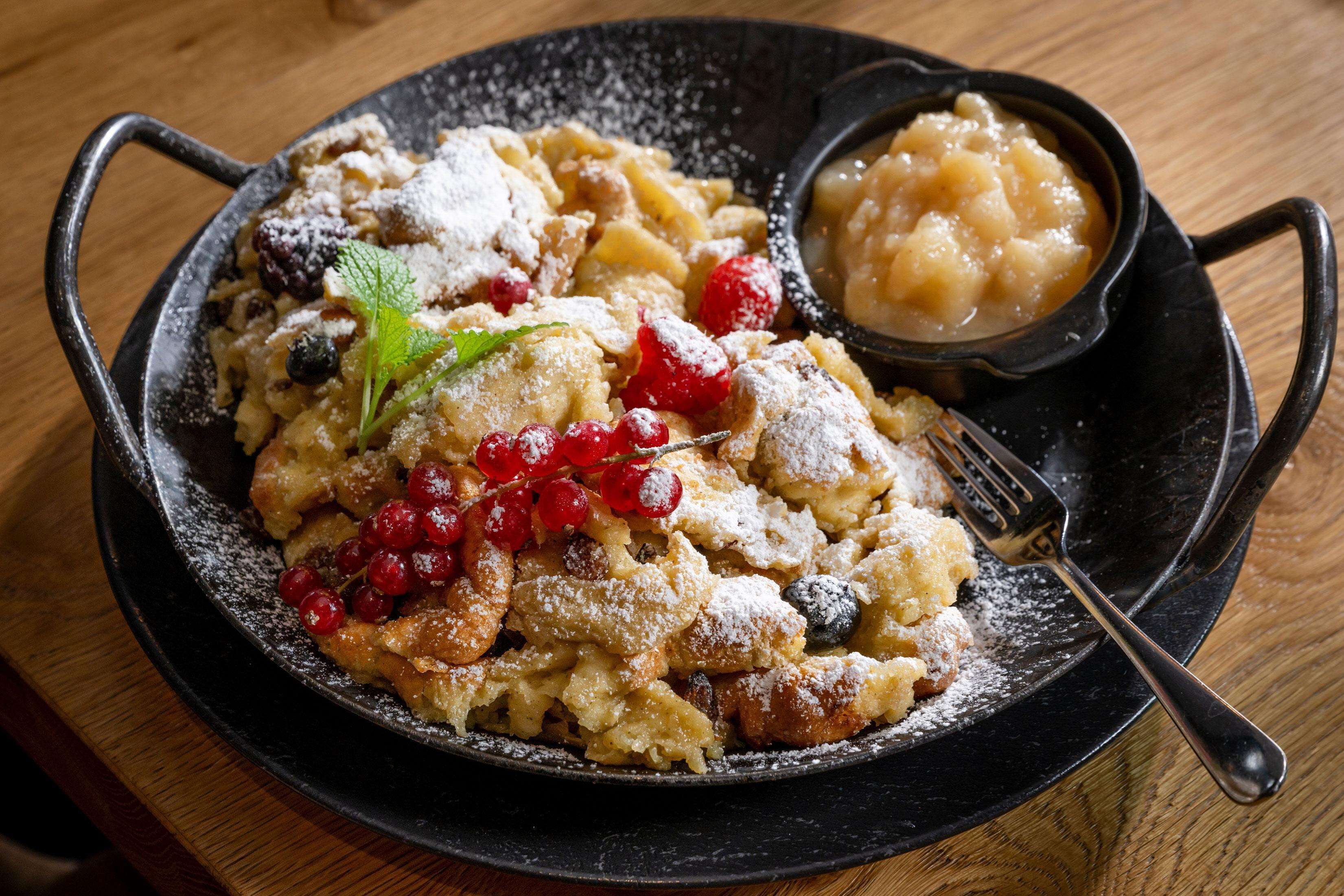 Une poêle noire contenant un dessert, peut-être des chaussons aux pommes, et un petit bol de sauce, le tout posé sur une table en bois.