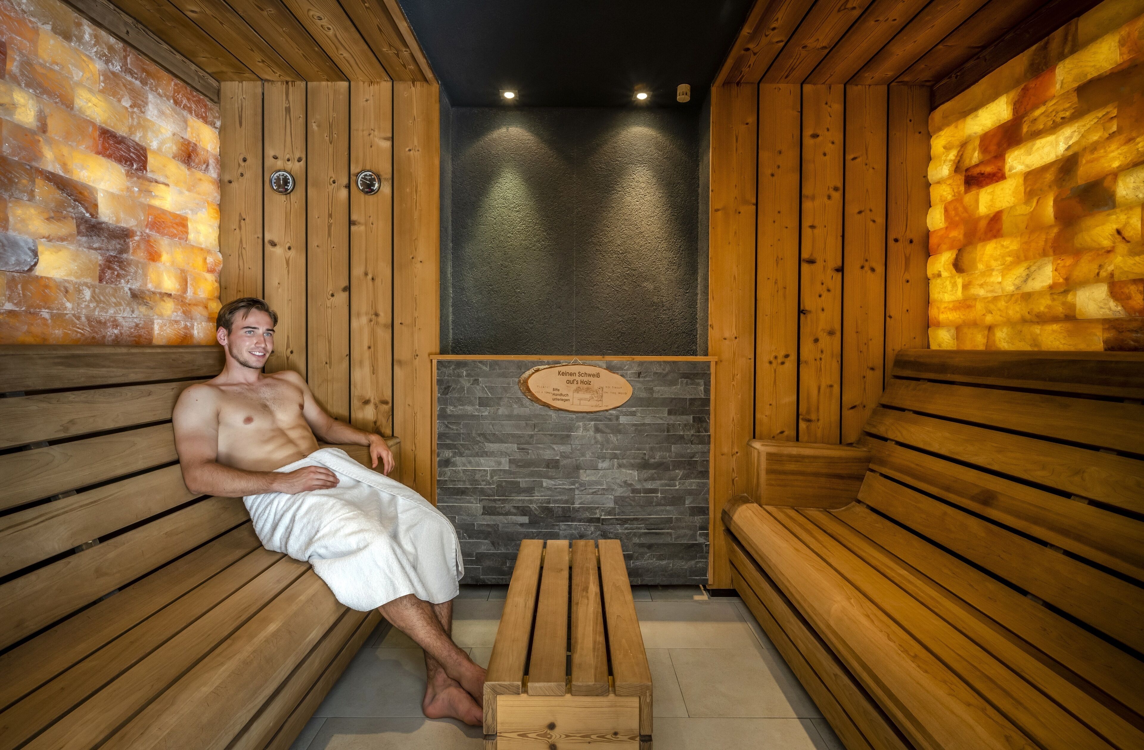 Un sauna avec des bancs en bois et un mur en pierre, une plaque portant une inscription et un banc en bois au centre.