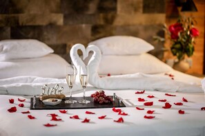 A neatly arranged bed with white linens, a tray with two glasses of champagne, a heart-shaped towel, and scattered rose petals. - Best Western Plus Hotel Erb (Vaterstetten)