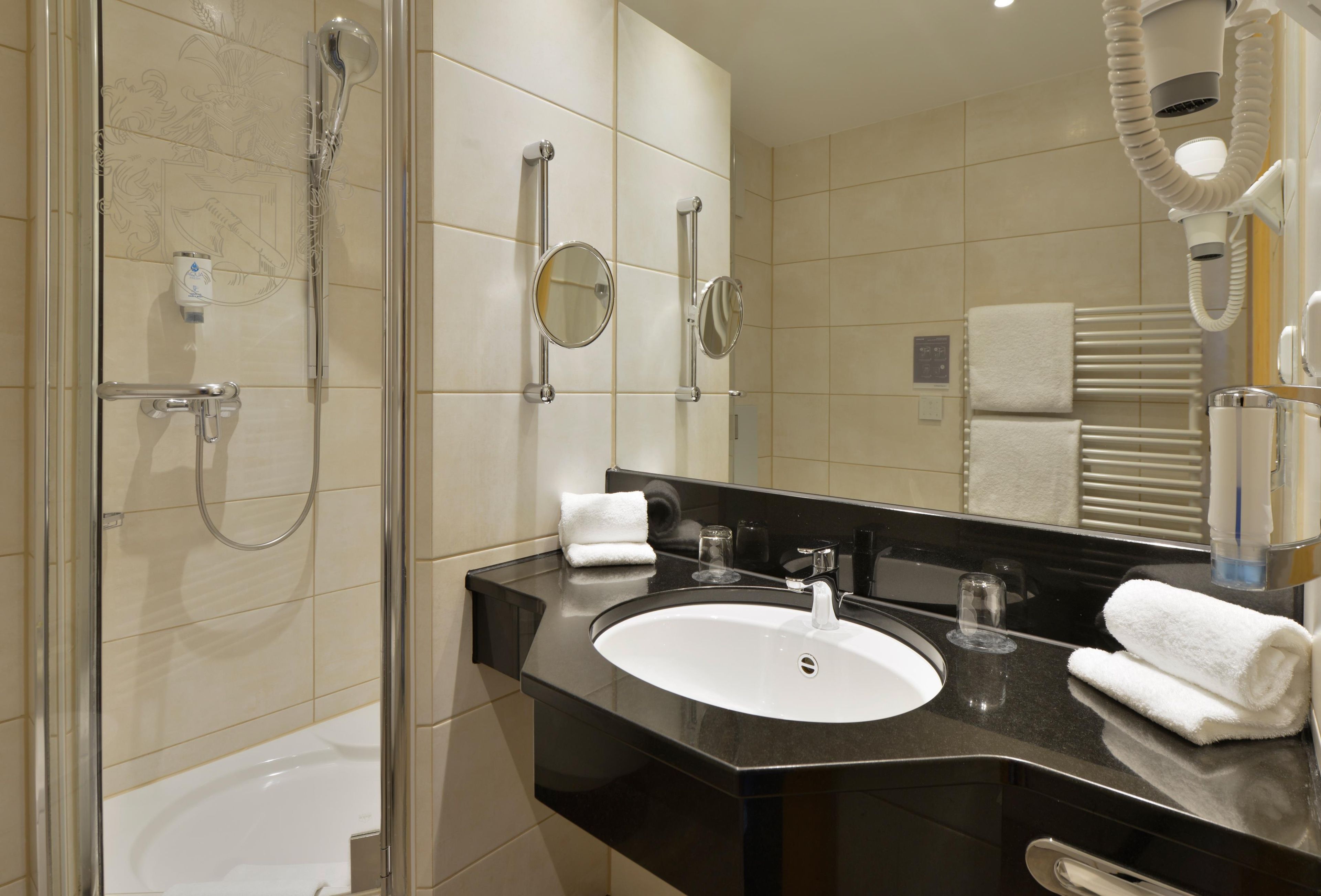 Une salle de bain moderne avec une douche à parois de verre, un lavabo sur un plan de travail noir et un miroir au-dessus du lavabo.