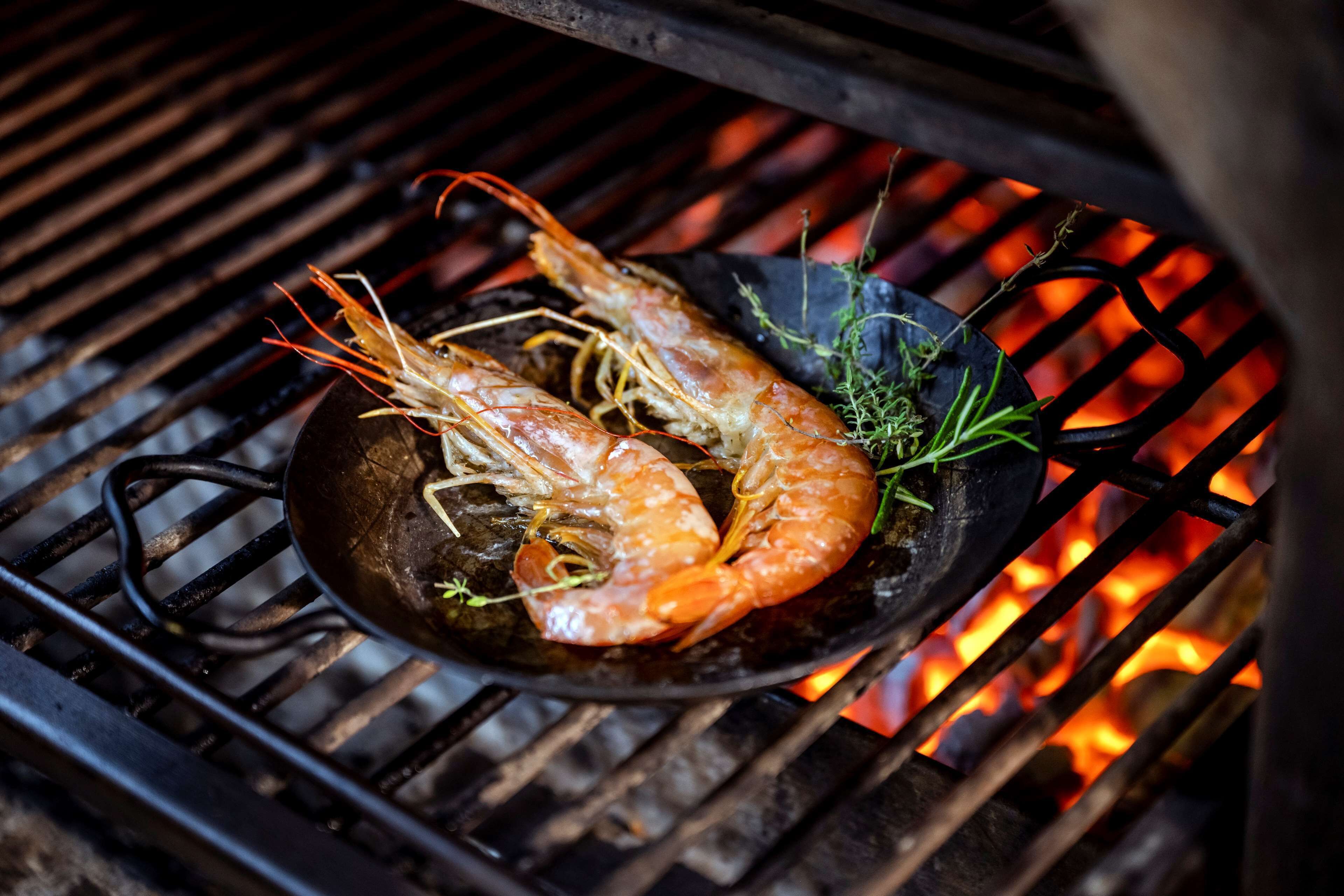 Deux crevettes grillées sur une plaque, au-dessus d’une flamme.