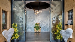 A hotel entrance with a modern design, featuring a glass door, a wooden reception desk, and a decorative plant arrangement. - Best Western Plus Hotel Erb (Vaterstetten)