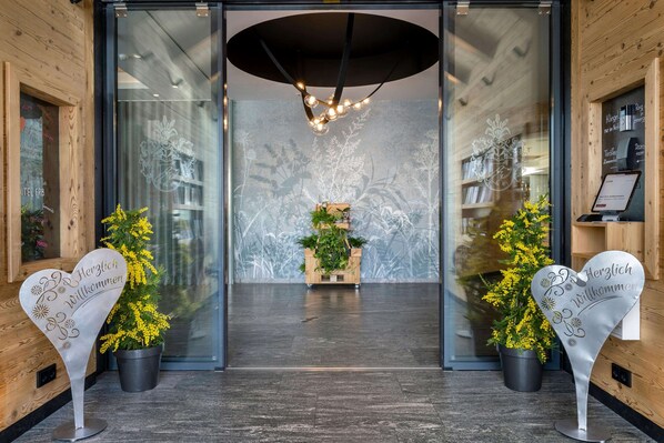 A hotel entrance with a modern design, featuring a glass door, a wooden reception desk, and a decorative plant arrangement. - Best Western Plus Hotel Erb (Vaterstetten)
