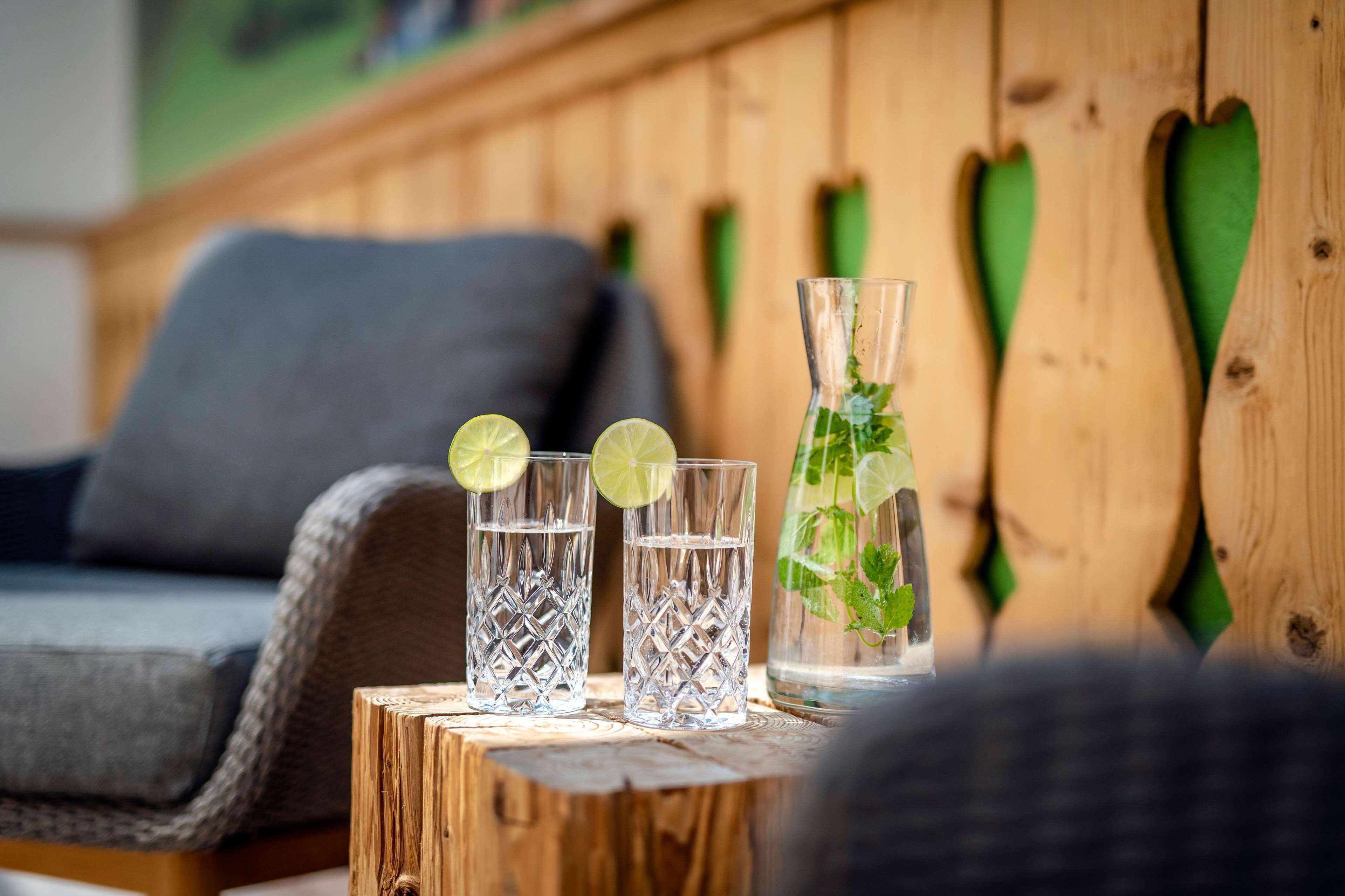 A wooden table with two glasses of water and a bottle of water with mint leaves, set against a wooden wall with heart-shaped cutouts.