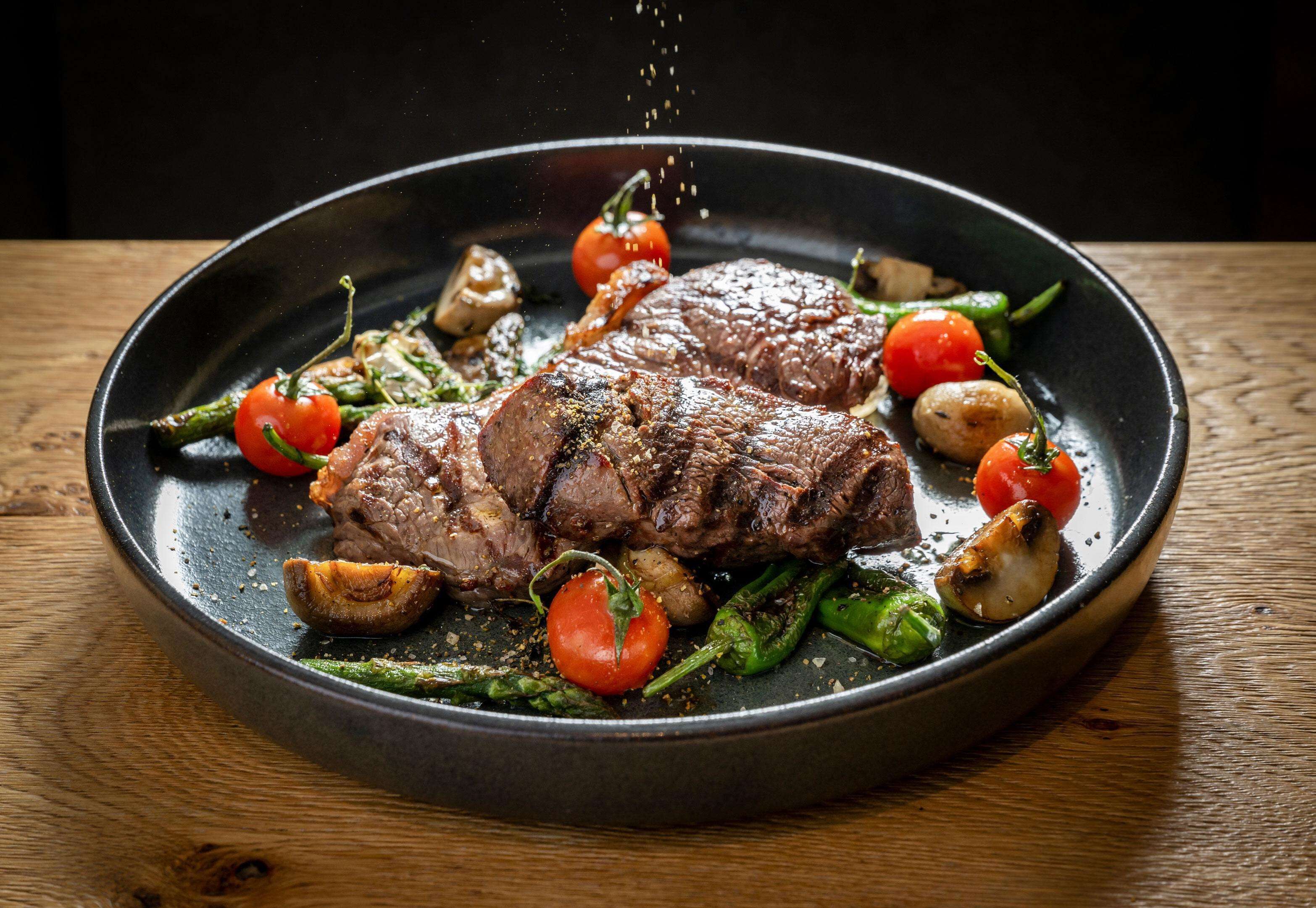 Ein Steak mit Gemüse auf einem dunklen Teller.