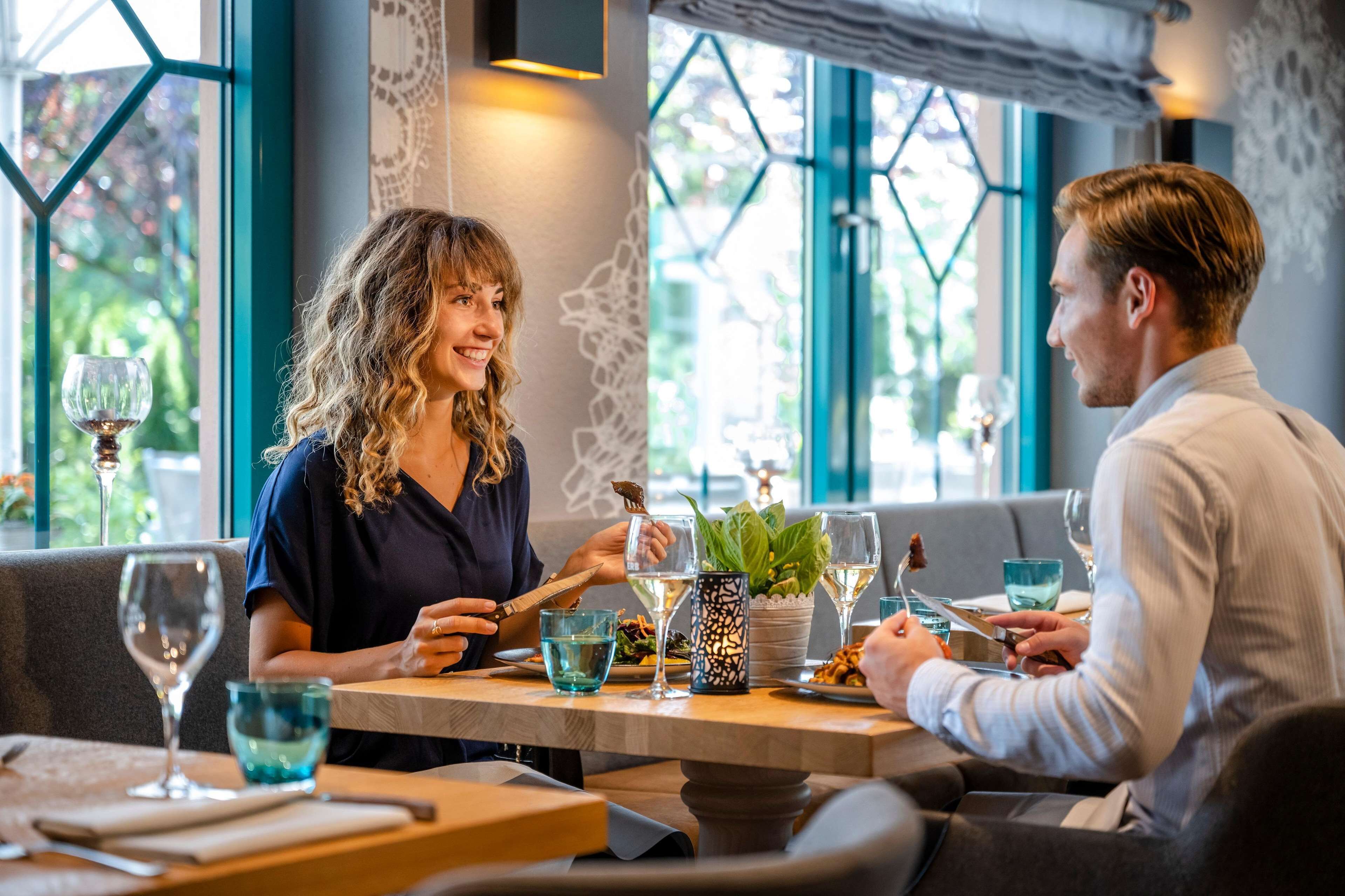 Een eethoek met een tafel gedekt voor twee personen, inclusief een potplant, wijnglazen en een menukaart.