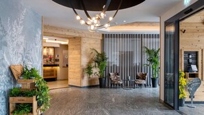 A modern lobby with a wooden reception desk, potted plants, and a seating area with chairs and a table. - Best Western Plus Hotel Erb (Vaterstetten)