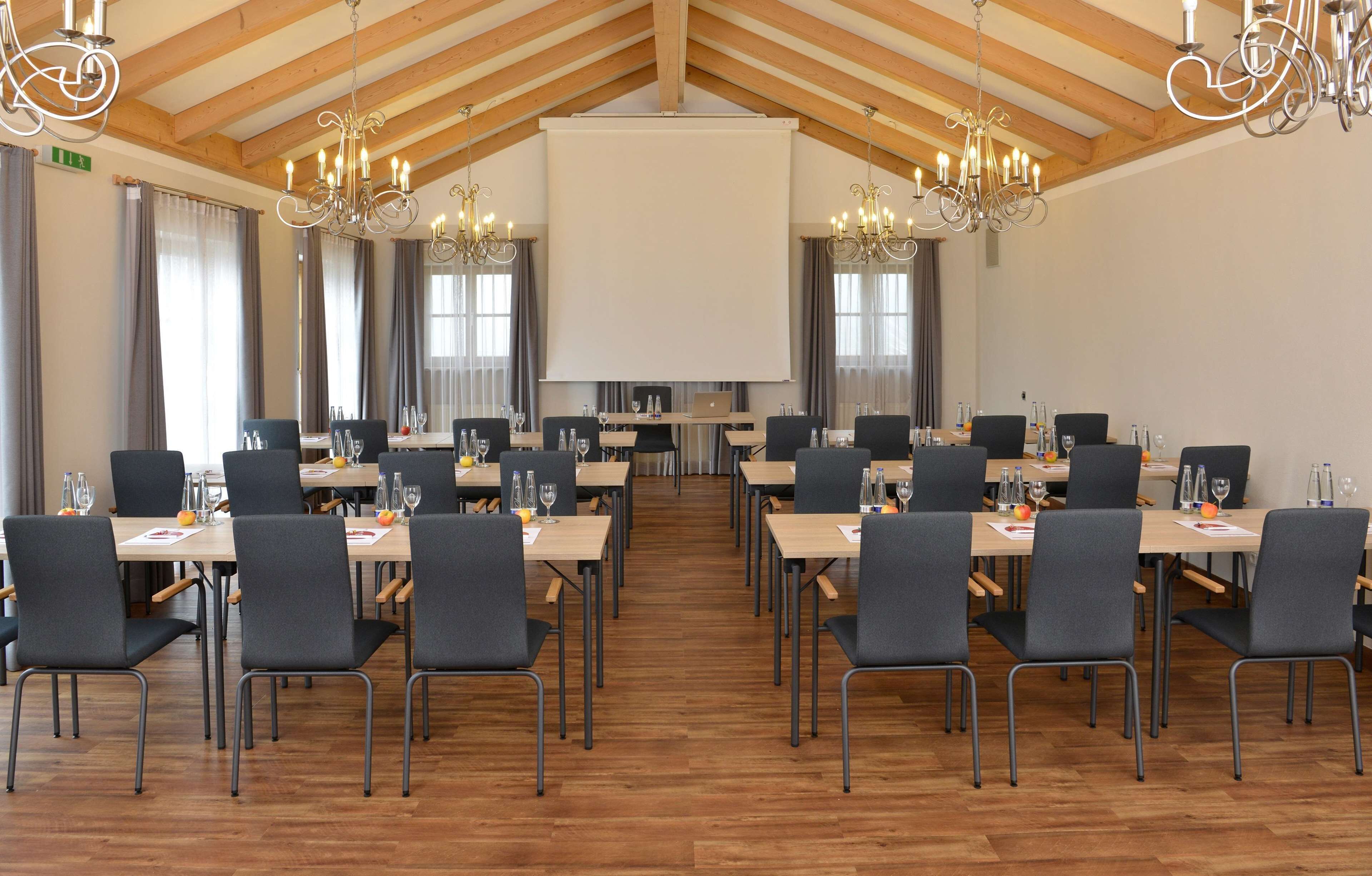 A conference room with multiple tables, chairs, and a large screen.