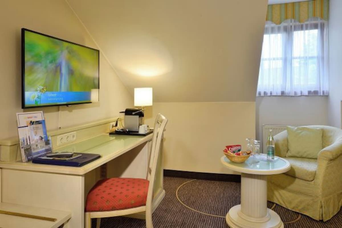 A hotel room with a desk, chair, television, lamp, and a small table with a bowl and bottles.