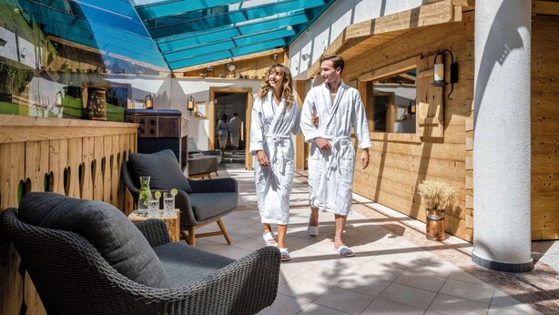 A spa area with wooden walls, a glass ceiling, and a seating area with wicker chairs and a small table. - Best Western Plus Hotel Erb (Vaterstetten)