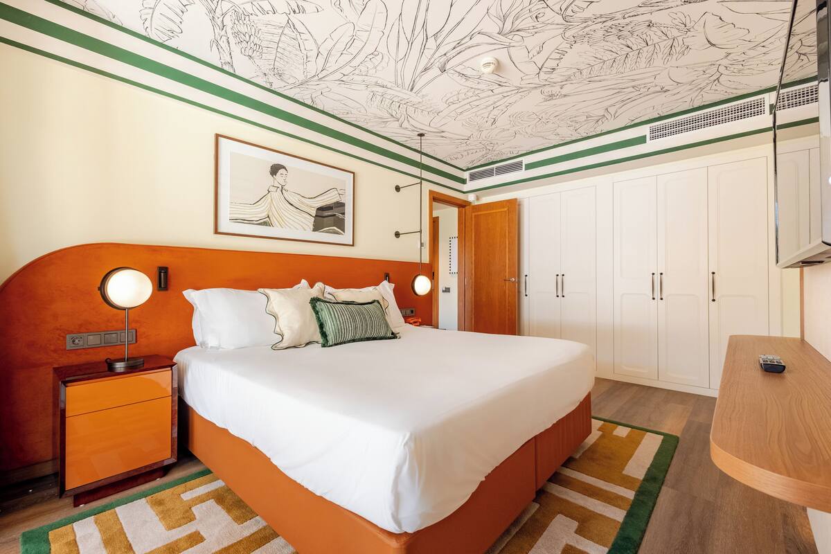 A bedroom with a bed, nightstand, bedside lamps, a framed picture on the wall, and a wardrobe.