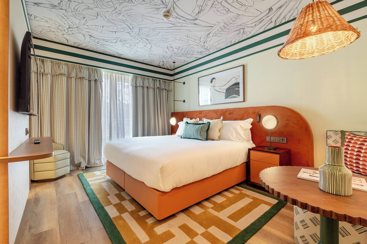 A hotel room with a bed, bedside table, lamp, and a decorative vase.