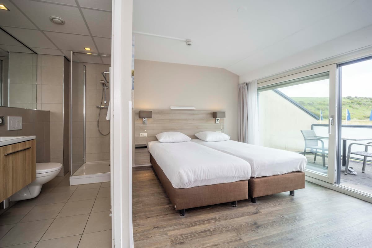 Una habitación de hotel moderna con ducha, inodoro y una cama con dos almohadas.