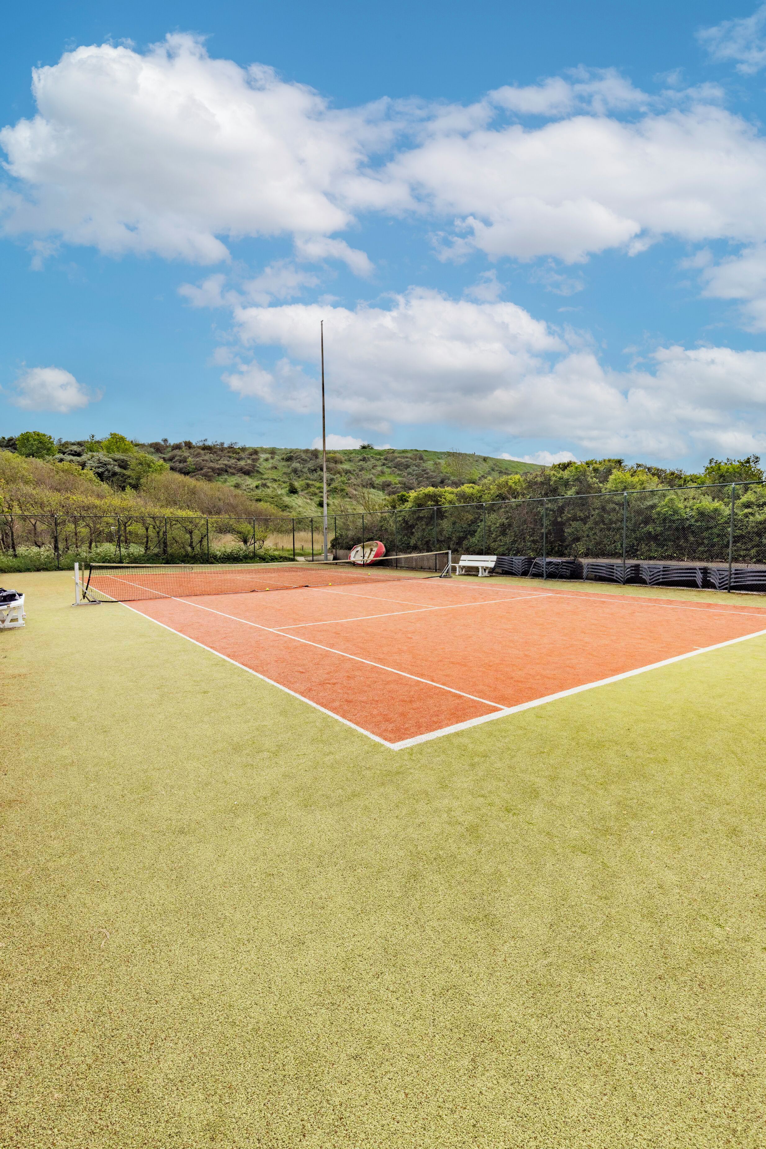 Un court de tennis avec un filet, entouré d’une clôture et d’arbres.