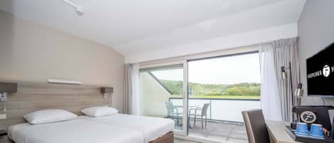 A hotel room with a large bed, a desk with a coffee machine, and a balcony with a view of the landscape.