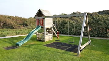 Explore a playground set amidst a beautifully landscaped garden, featuring a playhouse and a swing set.