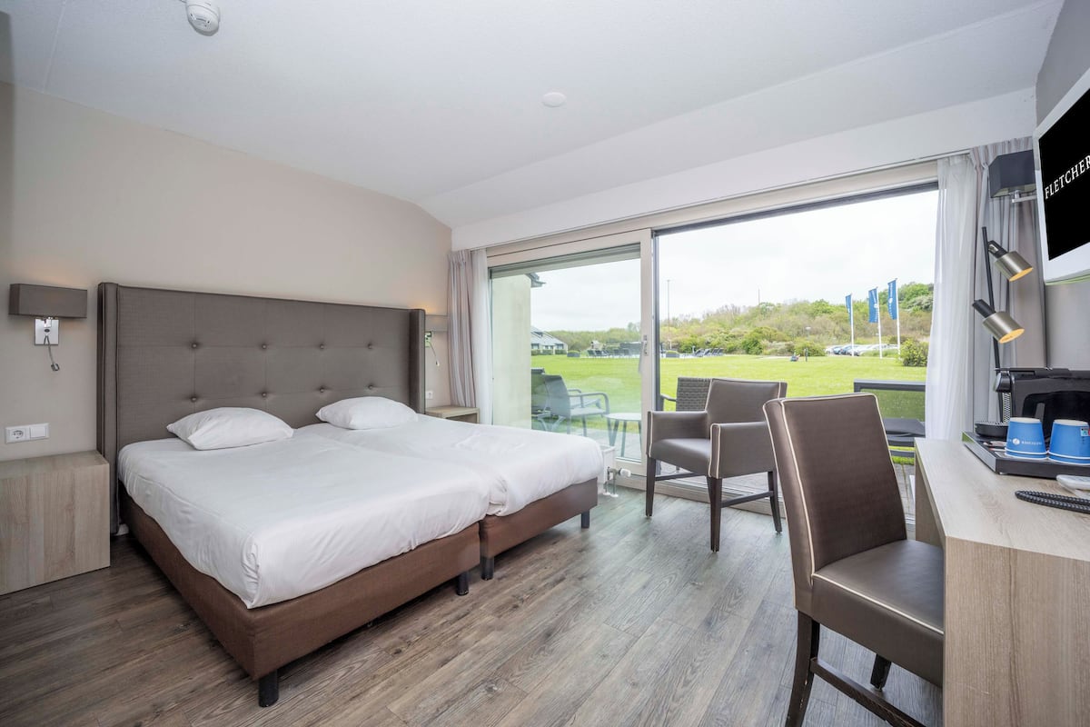 Habitación de hotel con una cama grande, un escritorio con computadora y vistas a un campo de golf.