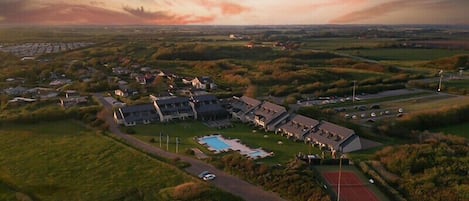 Vista aérea de un resort con varias edificaciones, una piscina y una cancha de tenis.