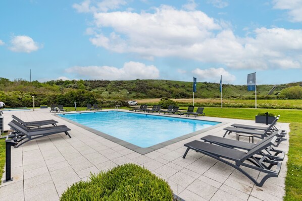 A swimming pool with lounge chairs and a flag. - Fletcher Zuiderduin Beachhotel (Westkapelle)