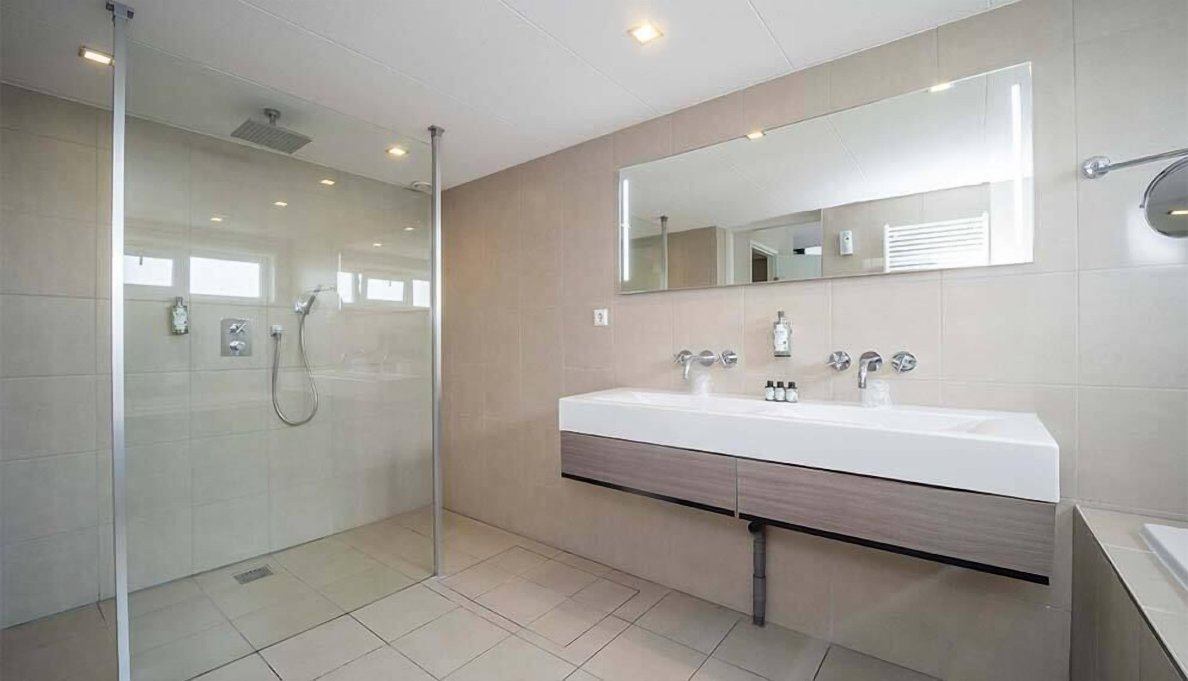 A modern bathroom with a glass shower enclosure, a large mirror, and a white sink with a wooden vanity.