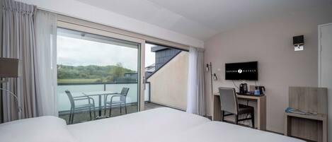 A hotel room with a large bed, a desk, a chair, a TV, and a balcony with a view of the outdoors.