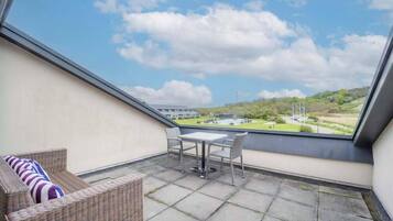Ein Balkon mit einem Korbsessel, einem kleinen Tisch und Stühlen mit Blick auf eine Rasenfläche und Gebäude.