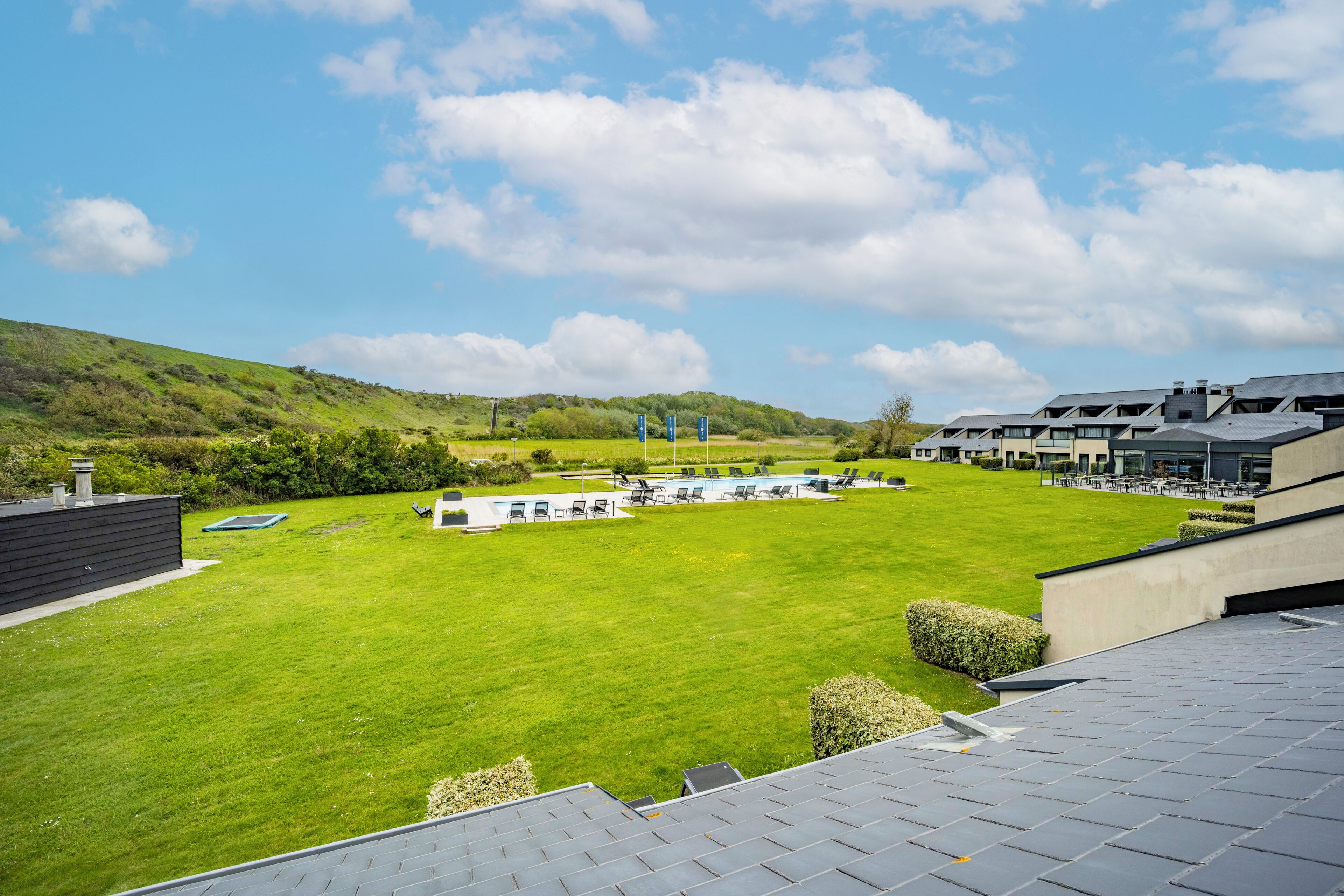 A hotel with a swimming pool, outdoor seating, and a view of the surrounding hills.