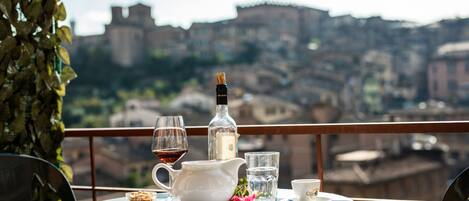 A table set with a bottle, glasses, a pitcher, and a cup, overlooking a historic cityscape.
