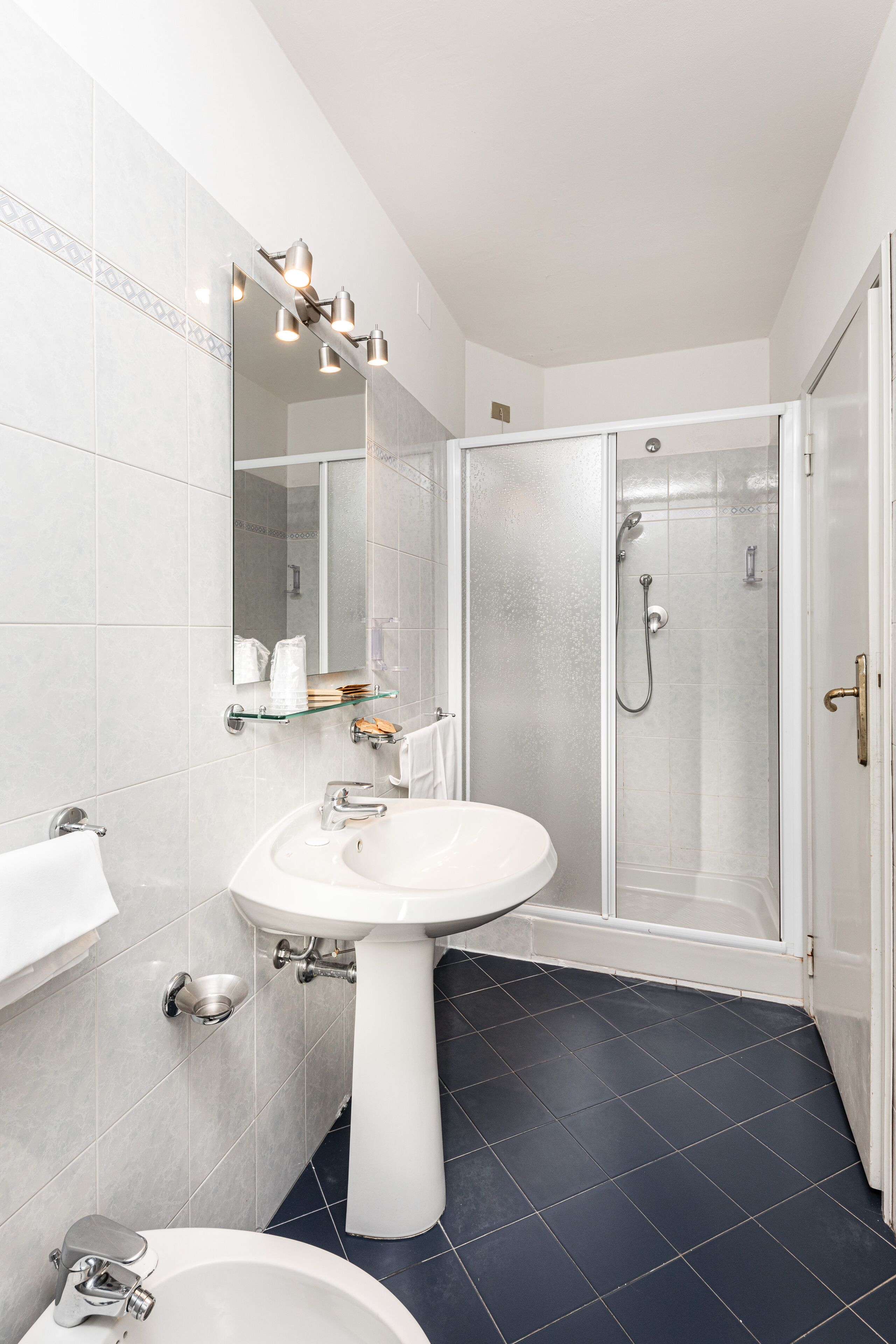 Un bagno moderno con lavabo su piedistallo, box doccia in vetro e un grande specchio con illuminazione.