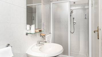 Un bagno moderno con lavabo su piedistallo, box doccia in vetro e un grande specchio con illuminazione.