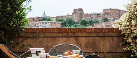 A table with breakfast items and a cup, overlooking a historic cityscape with buildings and a wall.