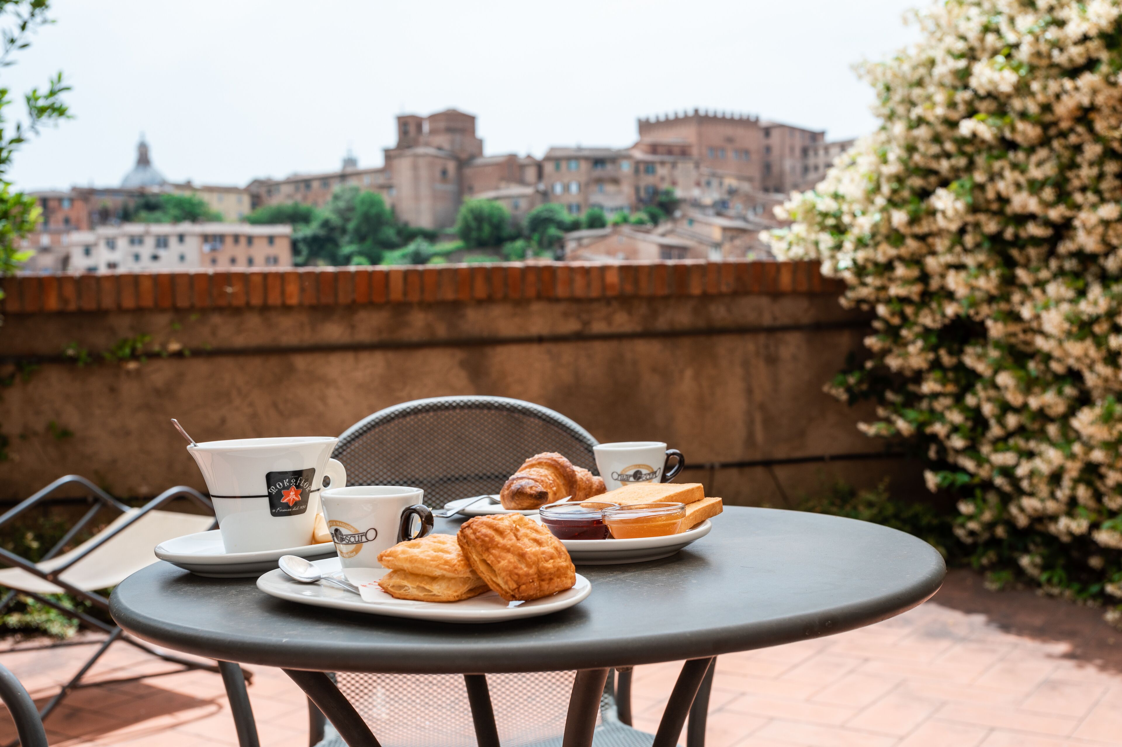 Una mesa con alimentos para el desayuno y vistas de edificios históricos al fondo.
