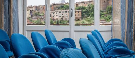 A room with blue chairs facing a window overlooking a cityscape with historic buildings.