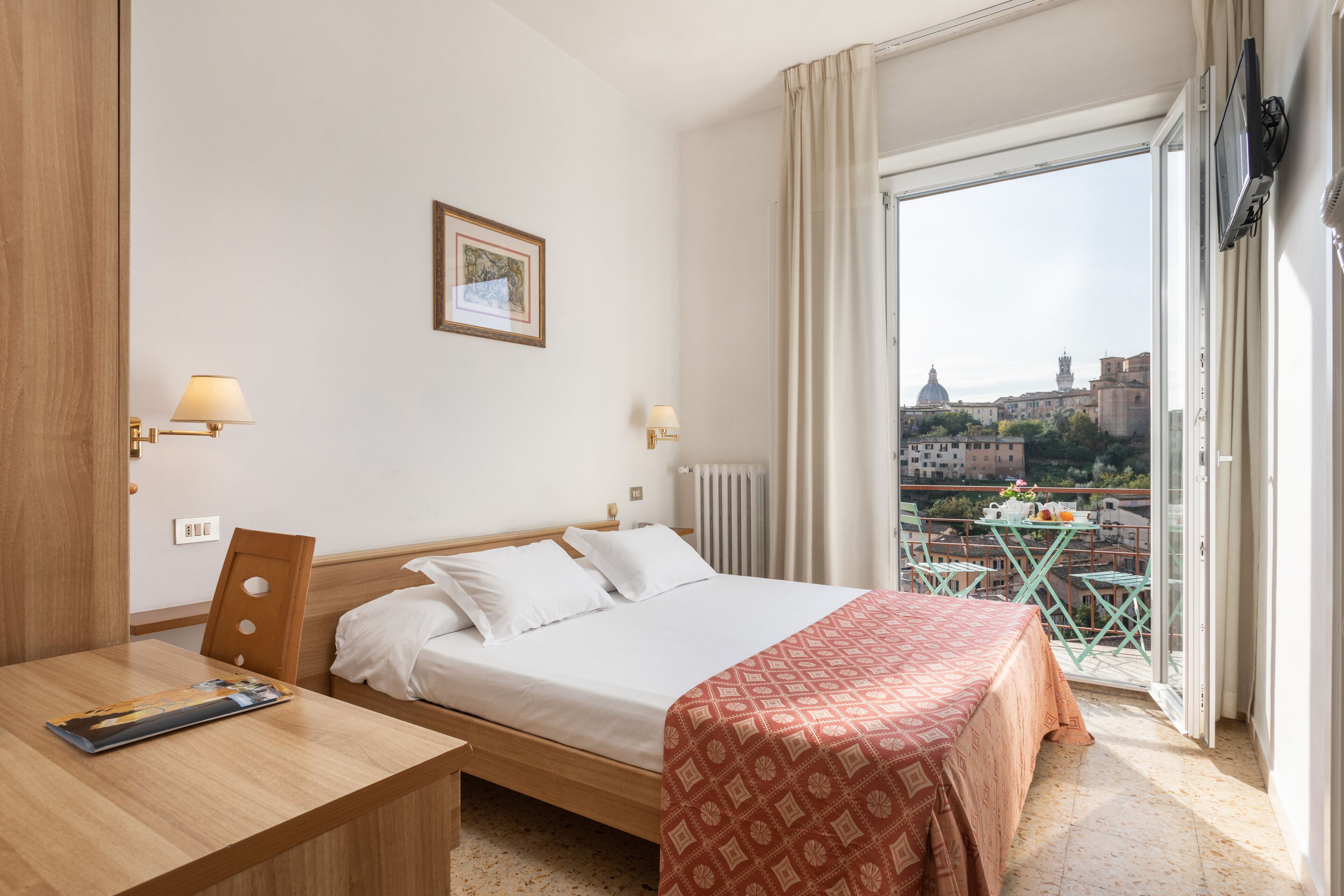 A hotel room with a bed, a table, and a balcony with a table and chairs.