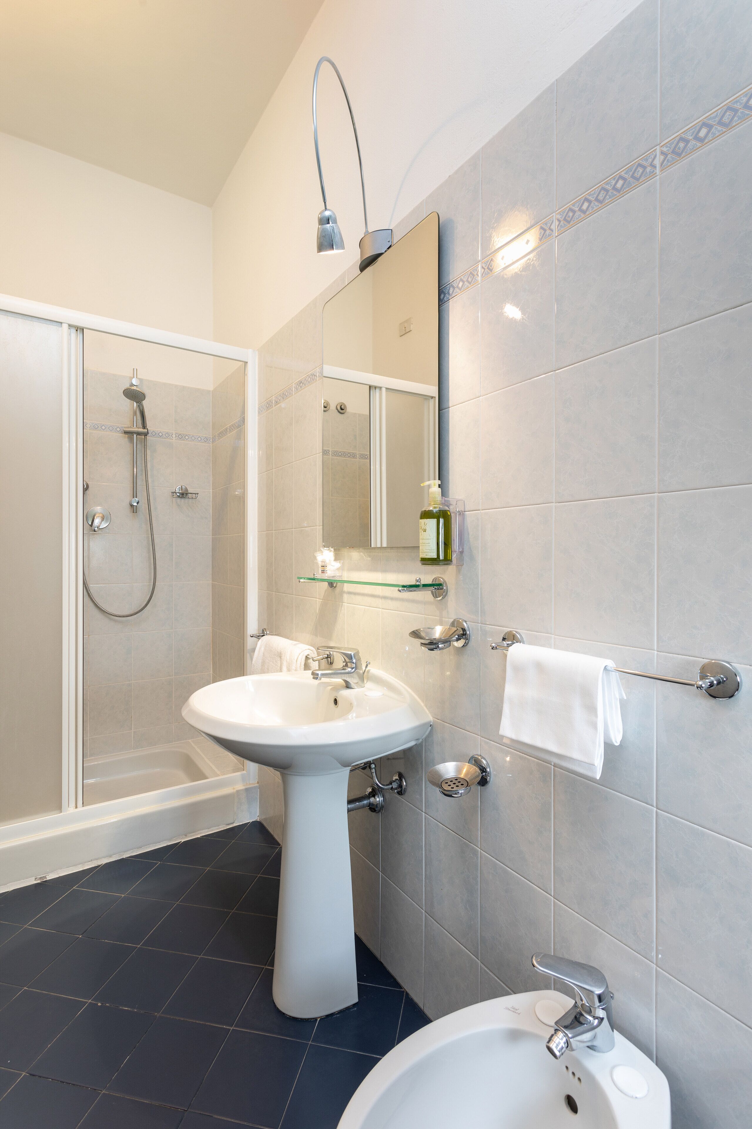 Un baño moderno con cabina de ducha de vidrio, lavamanos pedestal, espejo y toallero.