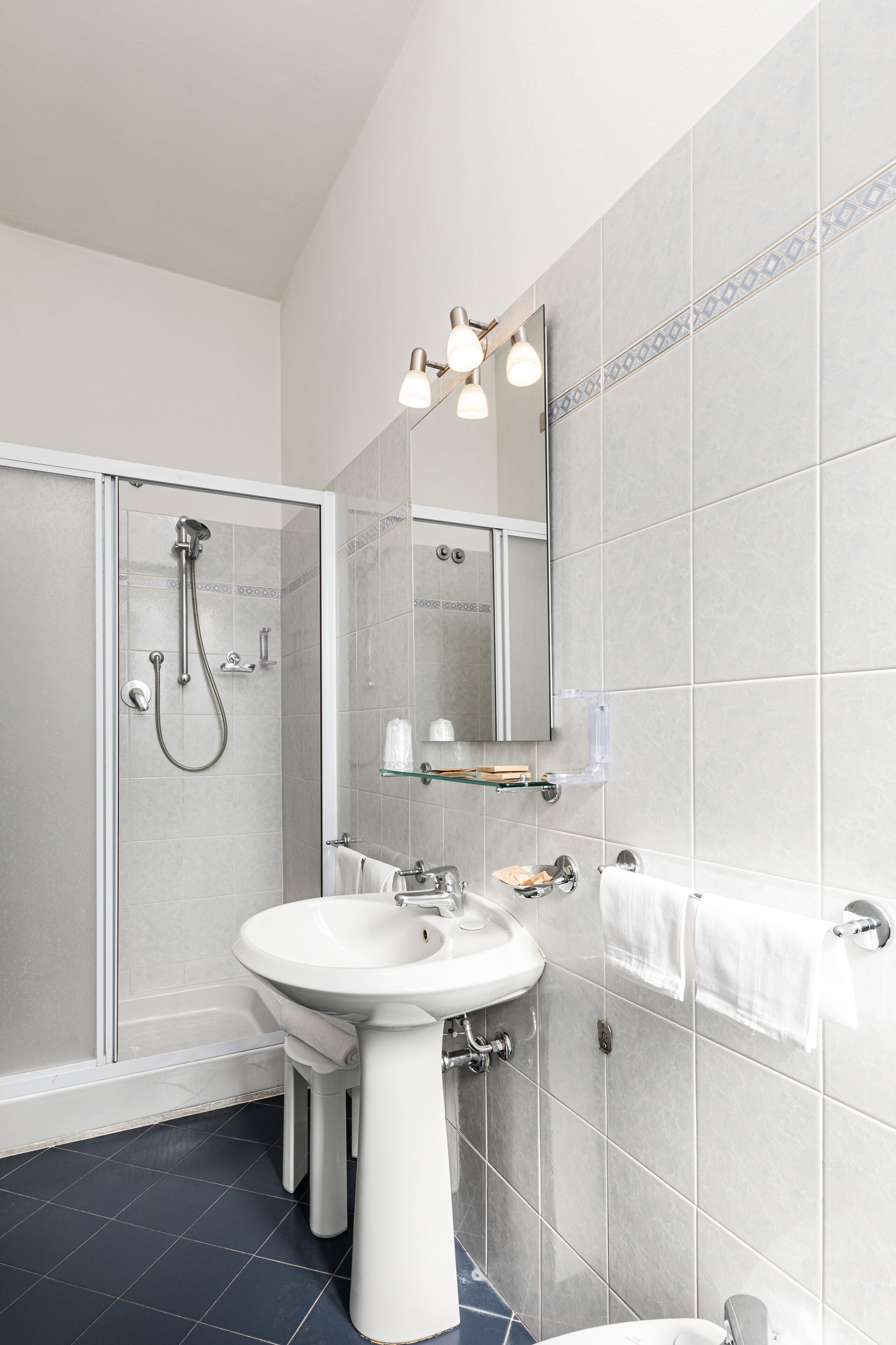 Een badkamer met een douche met glazen wand, een wastafel op voetstuk en een spiegel boven de wastafel.