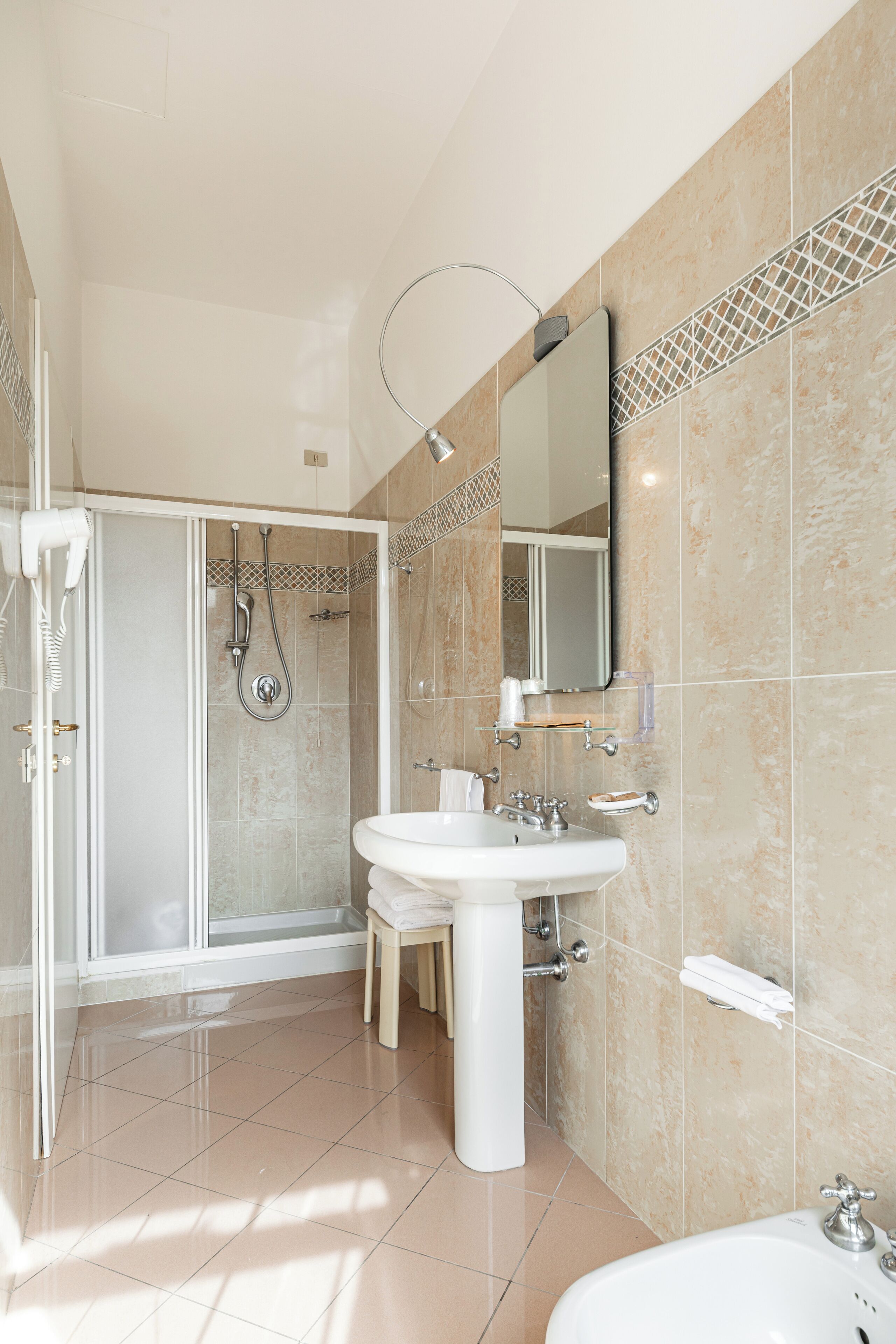 Un baño moderno con ducha de vidrio, lavamanos pedestal y un espejo grande.