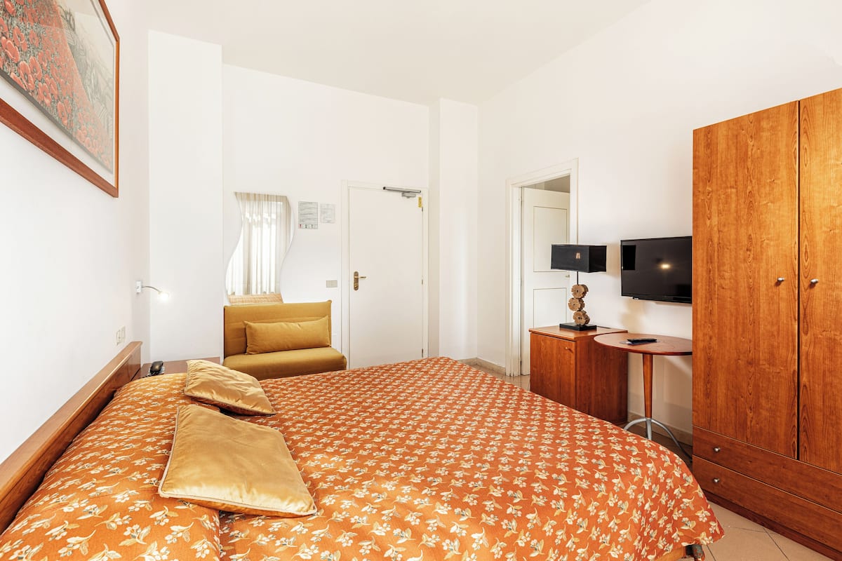 A hotel room with a bed, a sofa, a wardrobe, a TV, and a desk.
